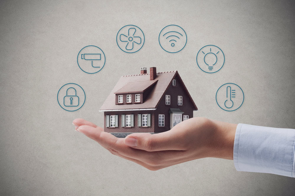A hand holds a small model house with icons surrounding it, representing various smart home technologies. The icons include a thermostat, light bulb, Wi-Fi signal, fan, lock, and roller brush, signifying automation and connectivity features. Ideal for those seeking Luxury Home Management in East Hampton.