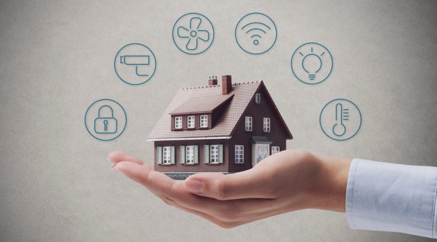 A hand holds a small model house with icons surrounding it, representing various smart home technologies. The icons include a thermostat, light bulb, Wi-Fi signal, fan, lock, and roller brush, signifying automation and connectivity features. Ideal for those seeking Luxury Home Management in East Hampton.